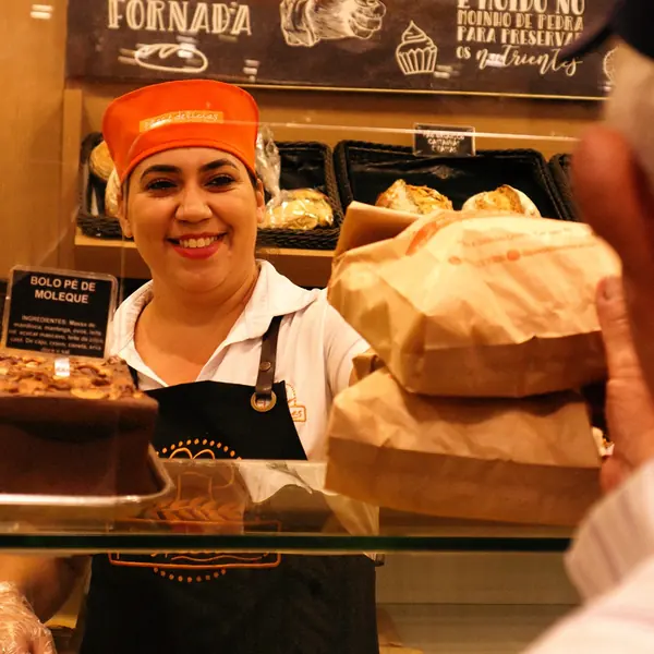 Atendente sorrindo no balcão de pães da Pães & Delícias