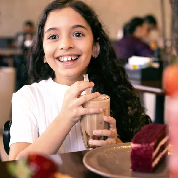 Menina sorrindo com bebida e doce na Pães & Delícias